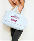 A woman holds a large light blue tote bag with the words 'LEBANON SOCIAL' and 'ANA W MY EMOTIONAL SUPPORT BAG' printed in dark red text against a plain white background.